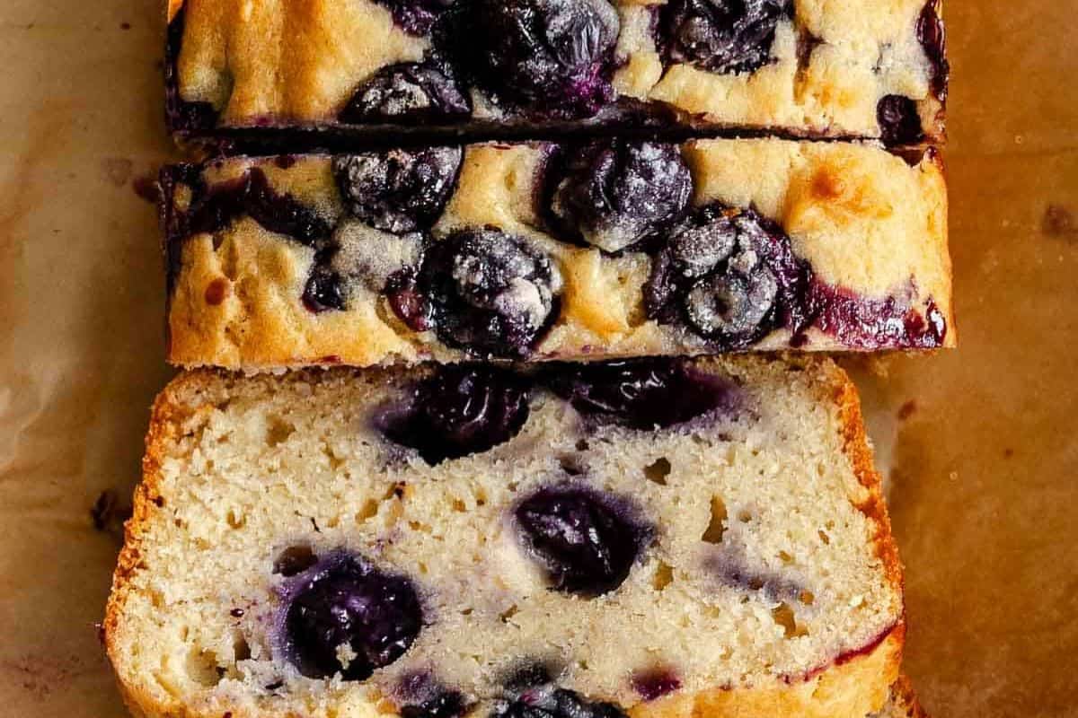Sliced blueberry loaf cake on parchment paper, showing visible blueberries inside and on top—one of the best quick breads to bake for easy recipes.