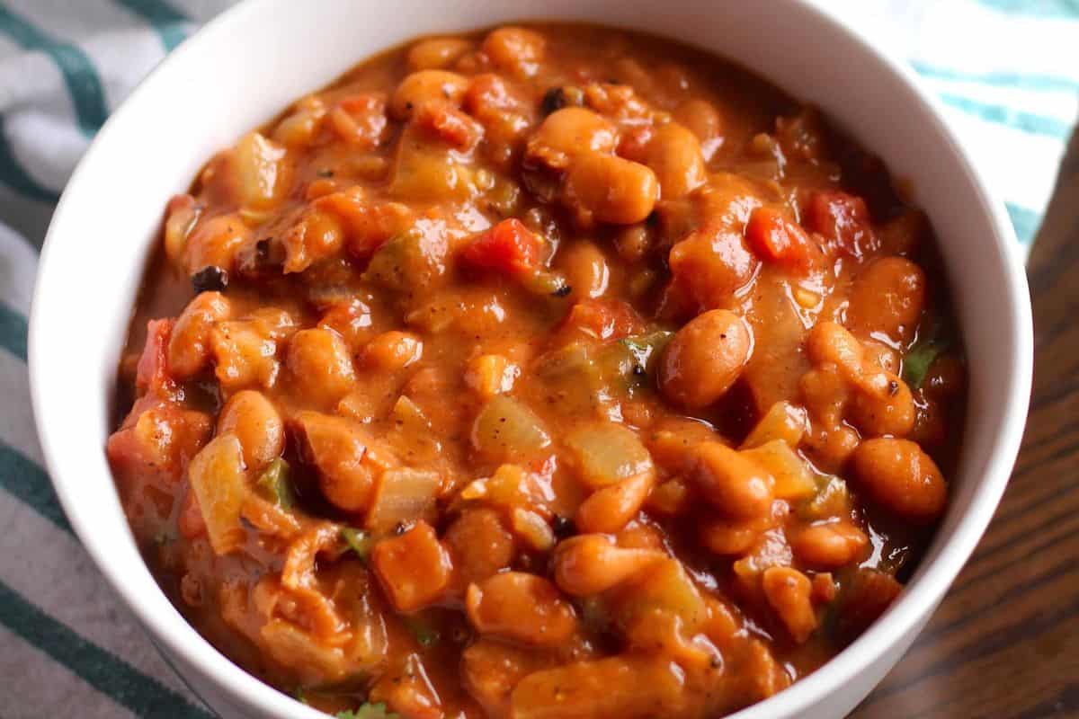 A white bowl filled with canned beans in a thick, tomato-based sauce with visible pieces of vegetables—one of those delicious dishes that's perfect for easy recipes.