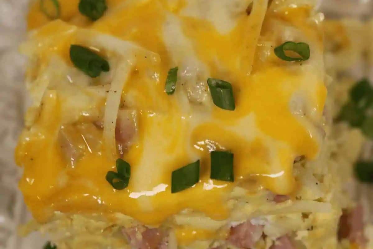 A close-up of a cheesy casserole topped with melted yellow and white cheese and chopped green onions.