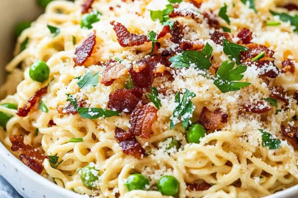 A plate of creamy pasta topped with crispy bacon pieces, green peas, grated cheese, and fresh parsley—an upgrade ramen twist for anyone craving flavor packed comfort food.