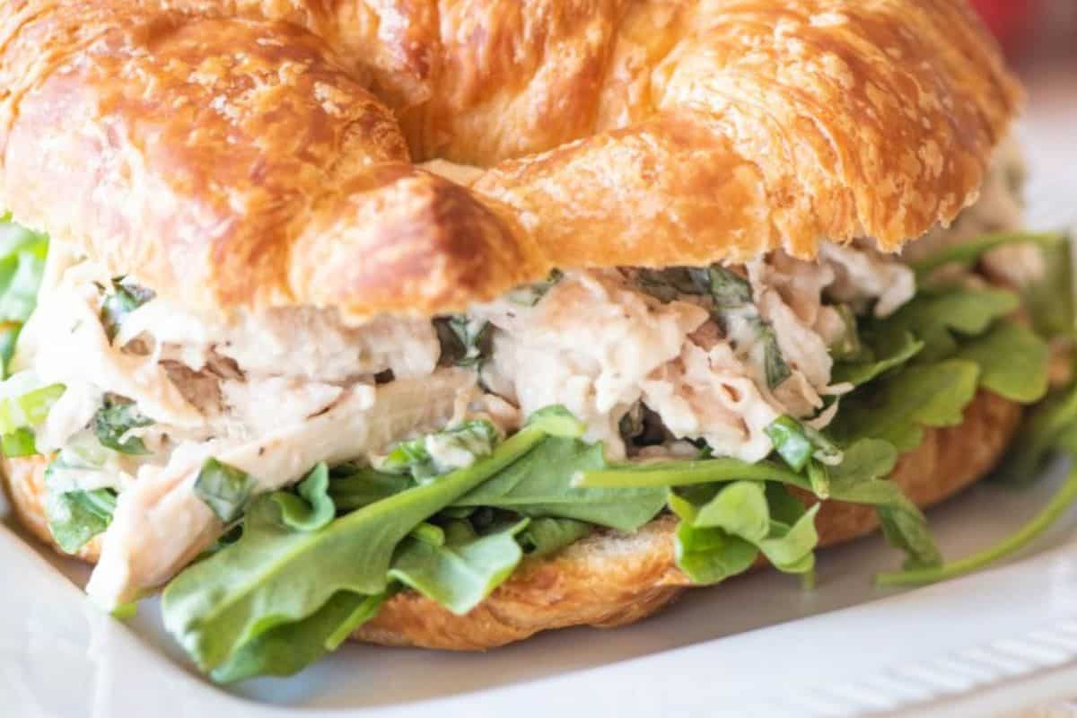  A chicken salad sandwich on a flaky croissant with green arugula leaves visible.