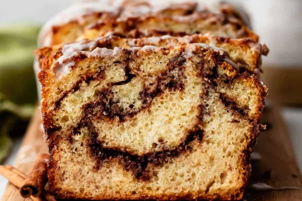 A close-up of sliced cinnamon swirl bread with a glaze on top, showing the cinnamon layers inside—this must-try treat is perfect for fans of quick breads.
