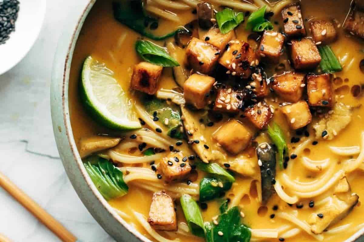 Bowl of flavor packed ramen with tofu cubes, bok choy, lime wedge, green onions, and black sesame seeds in a creamy broth—an easy ramen recipe to upgrade your next meal.