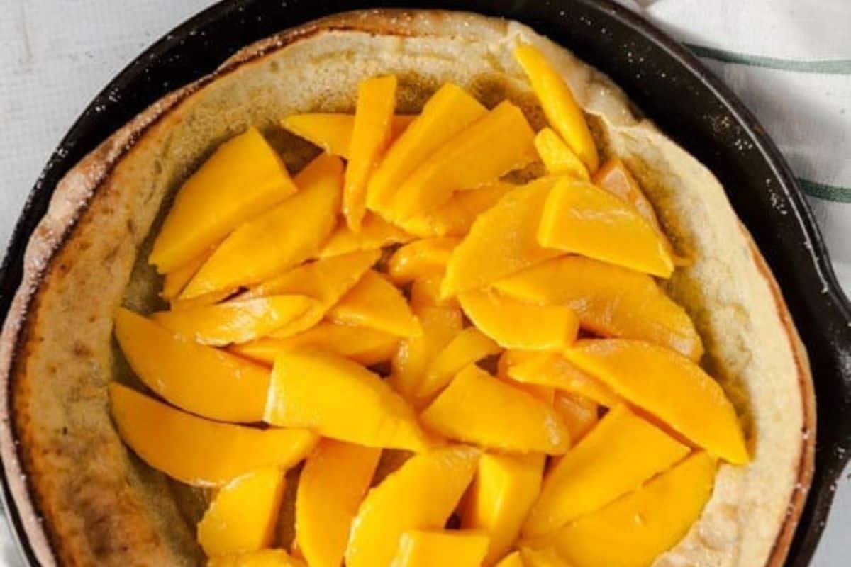 A delicious baked crust topped with sliced fresh mango pieces and a hint of fresh lime, served in a round black pan—perfect for cooking enthusiasts.