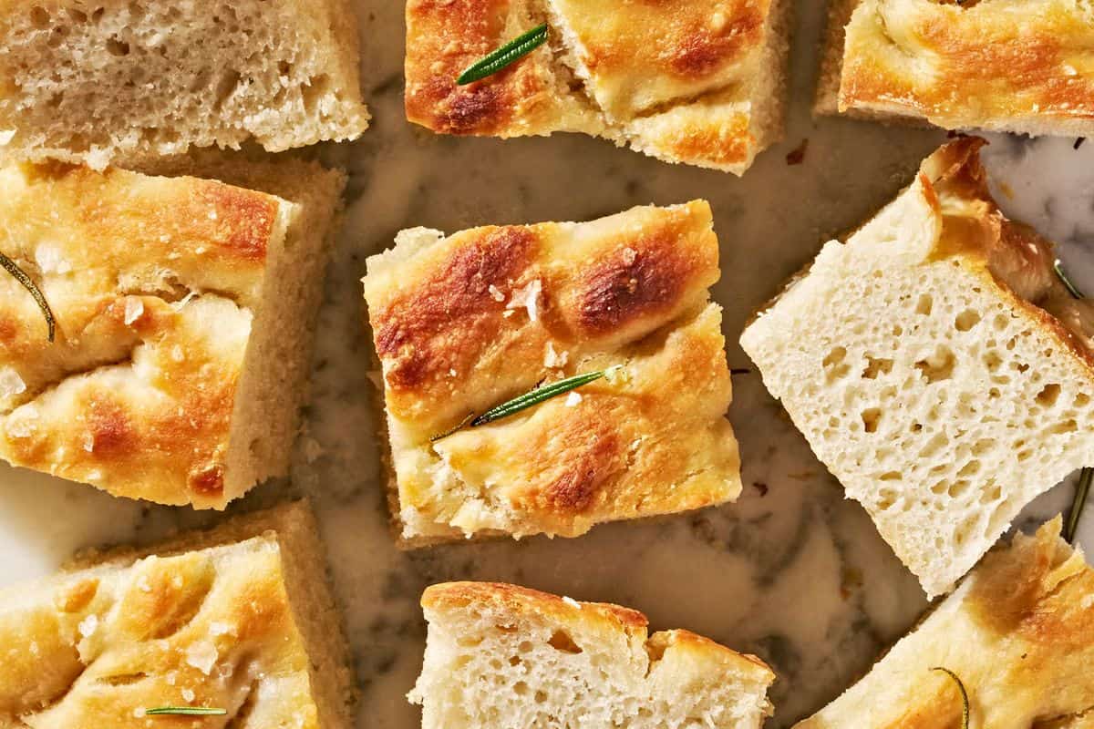Close-up of several square pieces of golden-brown focaccia bread, some topped with rosemary, on a light surface—a must try for fans of quick breads you can bake anytime.