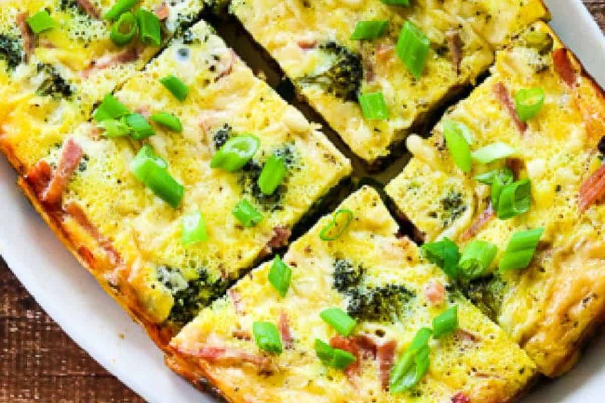A plate of sliced baked egg casserole, perfect for busy mornings, topped with chopped green onions and visible pieces of broccoli and ham.