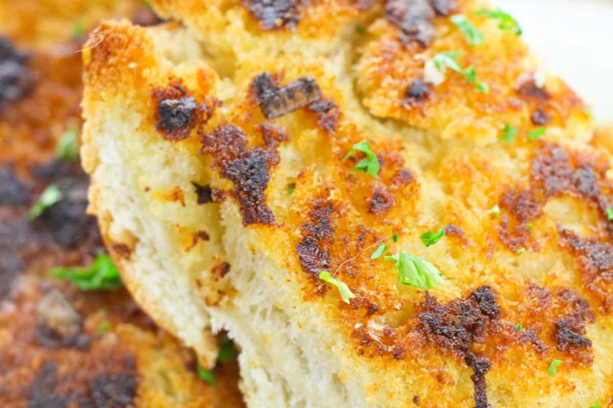 Close-up of golden-brown, crispy focaccia bread—an anytime favorite among quick breads—topped with herbs and charred bits fresh from the bake.