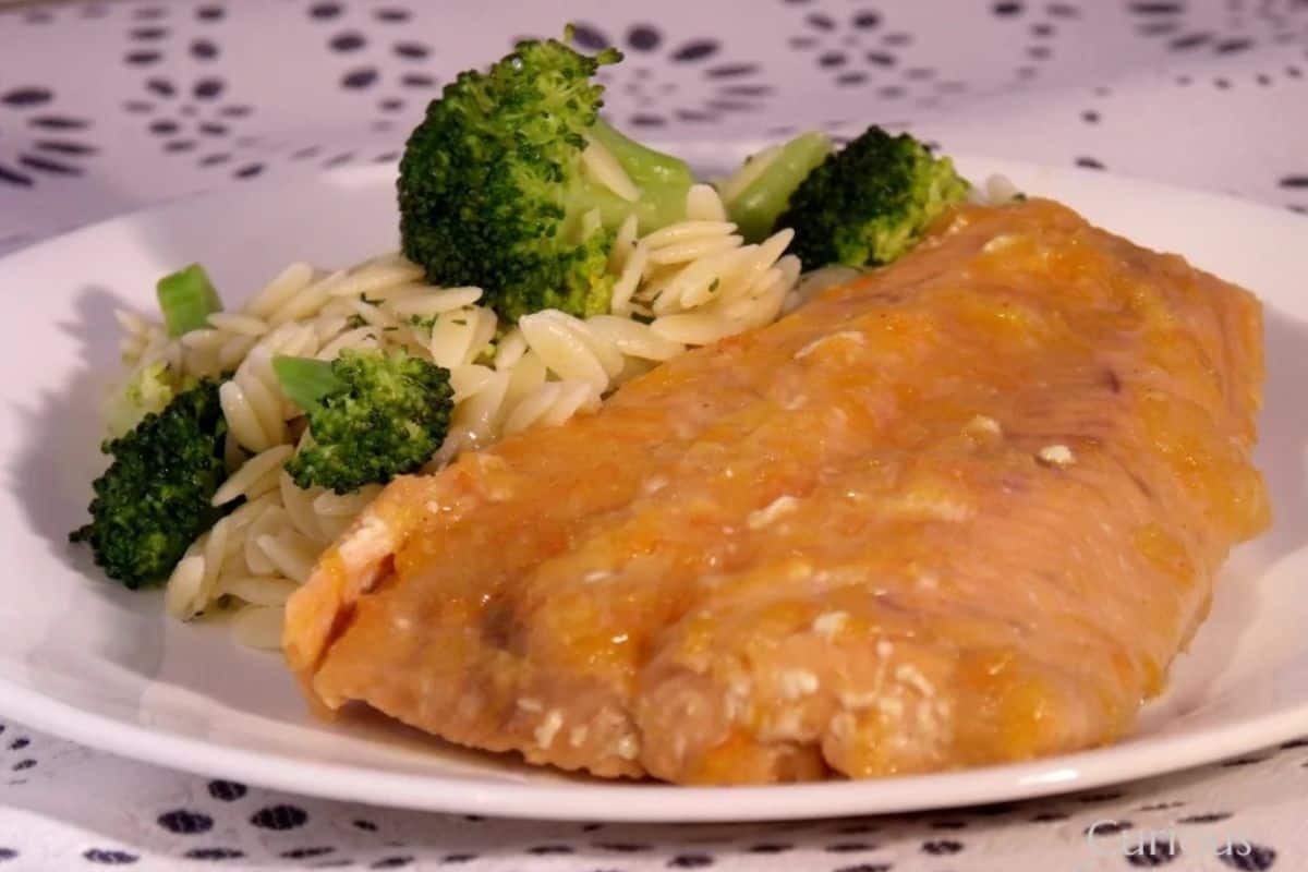 A cooked salmon fillet is served on a white plate with orzo pasta, broccoli florets, and a hint of fresh grapefruit for a vibrant twist.