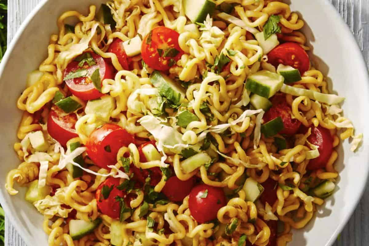 A bowl of flavor packed ramen noodle salad with cherry tomatoes, cucumber, shredded cabbage, and fresh herbs.