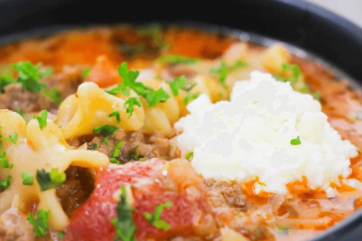 Close-up of a bowl of lasagna soup, a comforting soup topped with a dollop of ricotta cheese and garnished with chopped parsley—a delicious addition to your dinner recipes.