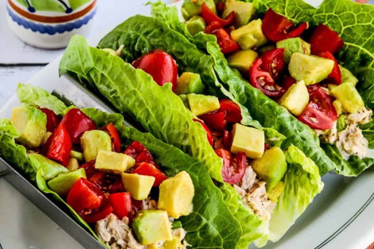 Three lettuce leaf wraps filled with tuna, diced avocado, and chopped tomatoes are displayed on a plate—an easy dinner idea for anyone looking for healthy recipes.
