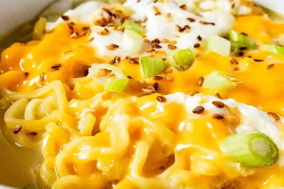 Close-up of cooked ramen noodles topped with melted cheese, sliced green onions, sesame seeds, and a drizzle of white sauce—a flavor packed ramen upgrade perfect for easy ramen recipes.