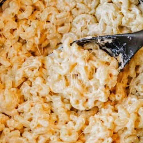 A close-up of creamy macaroni and cheese, a classic among Dutch oven recipes, being stirred with a black spoon.