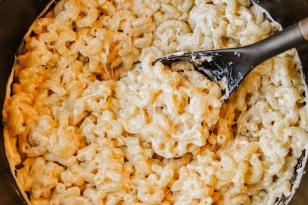 A close-up of creamy macaroni and cheese, a classic among Dutch oven recipes, being stirred with a black spoon.