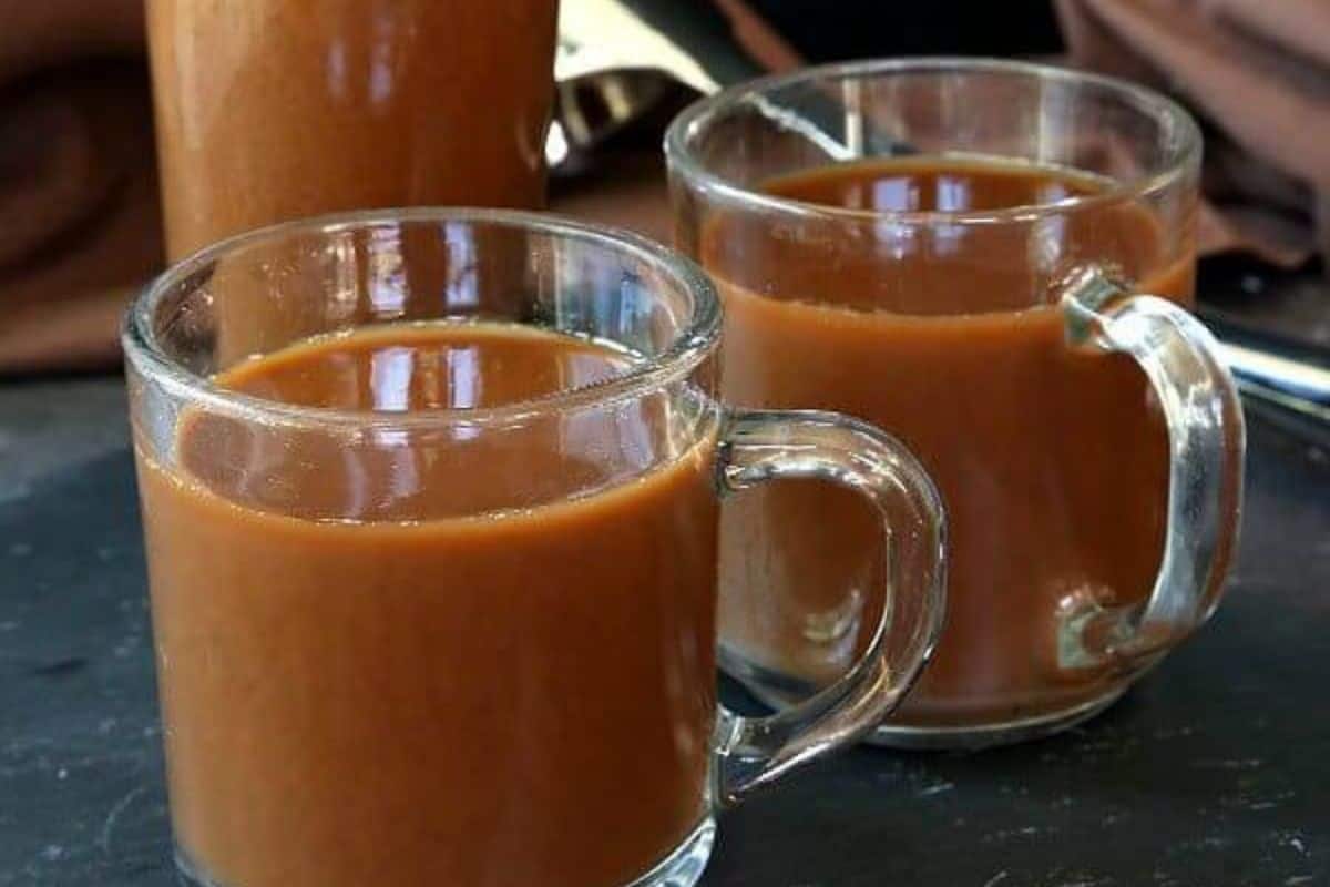 Two clear glass mugs filled with a brown beverage sit on a dark surface, with a glass bottle of the same drink in the background—perfect for cozy slow cooker breakfasts or fueling busy mornings.