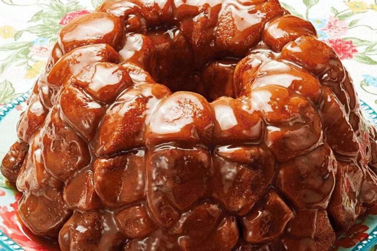 A glazed monkey bread ring sits on a floral-patterned plate, its pieces of baked dough coated in shiny caramel sauce—a must try for fans of quick breads you can bake anytime.