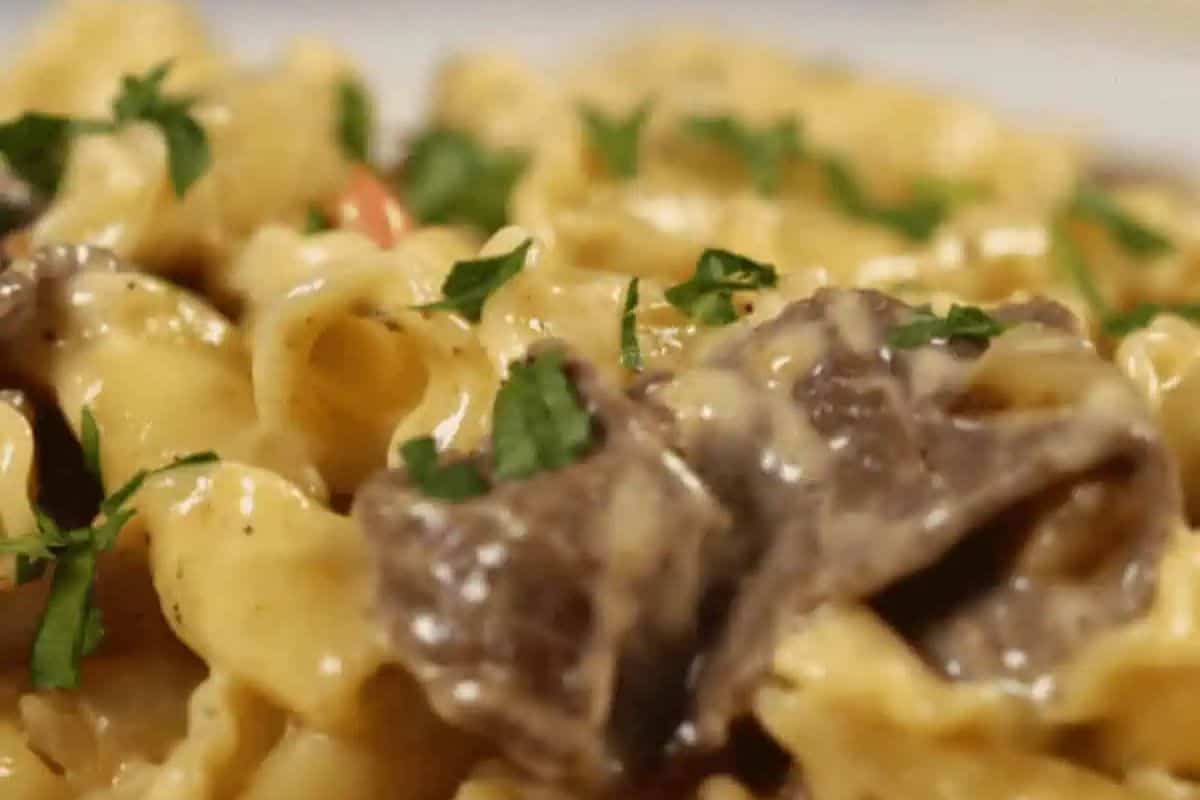 A close-up of pasta with a creamy sauce, chunks of meat, and garnished with fresh parsley. The pasta appears to be a cavatappi or similar shape.