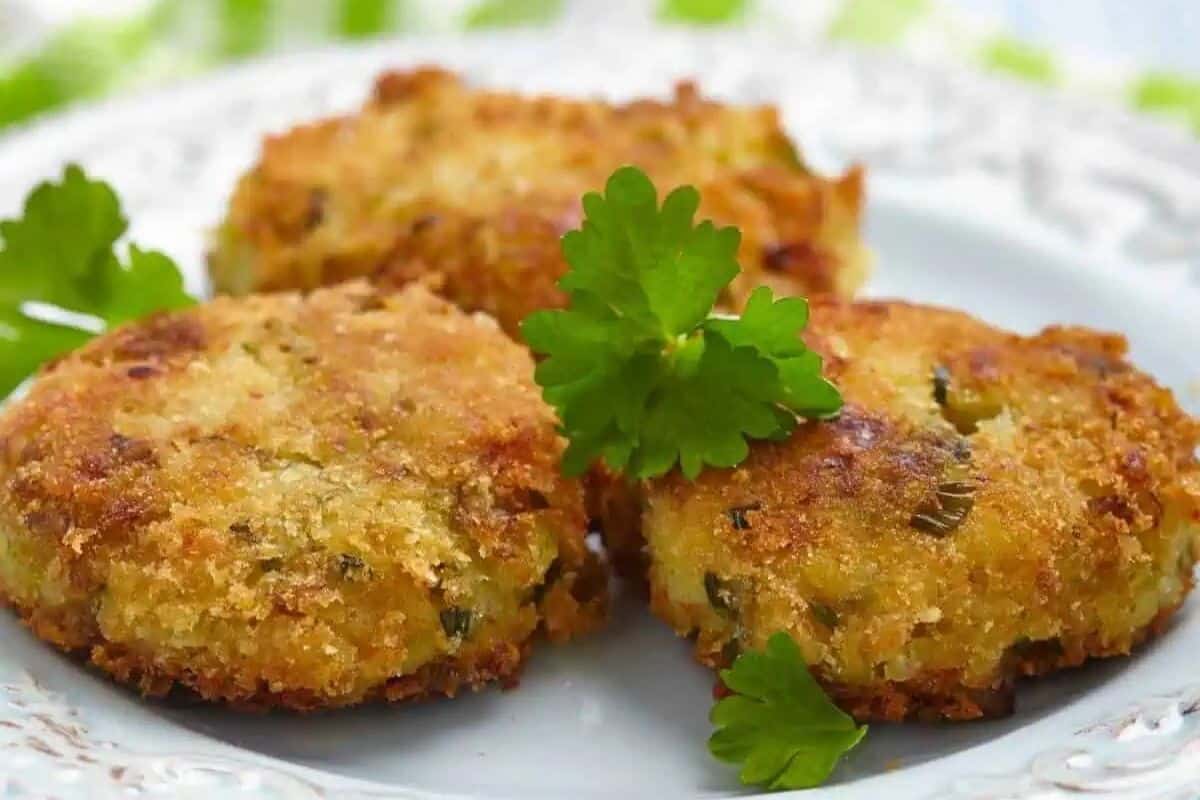 Three breaded and fried patties are arranged on a white plate, garnished with fresh parsley leaves—an easy tuna meal perfect for any canned tuna dinner lineup.