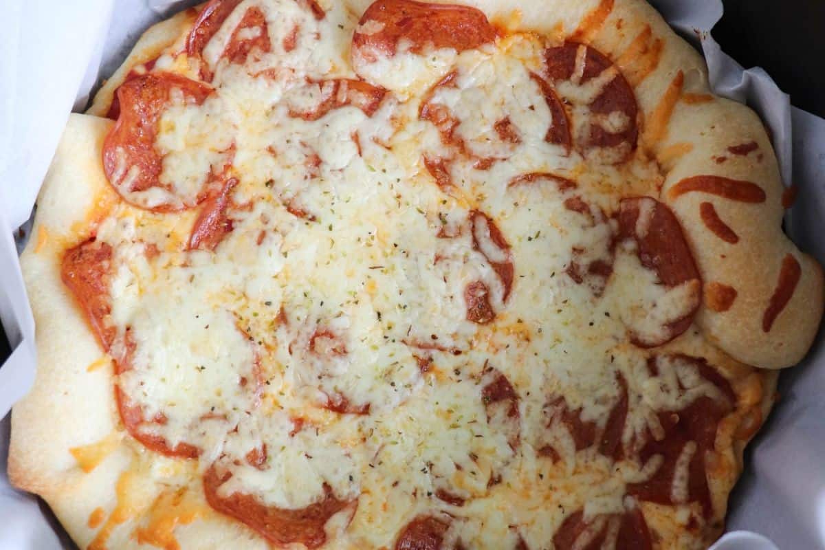 A baked pepperoni pizza with melted cheese on a thick crust, placed on white parchment paper—perfect for those who love hearty recipes.