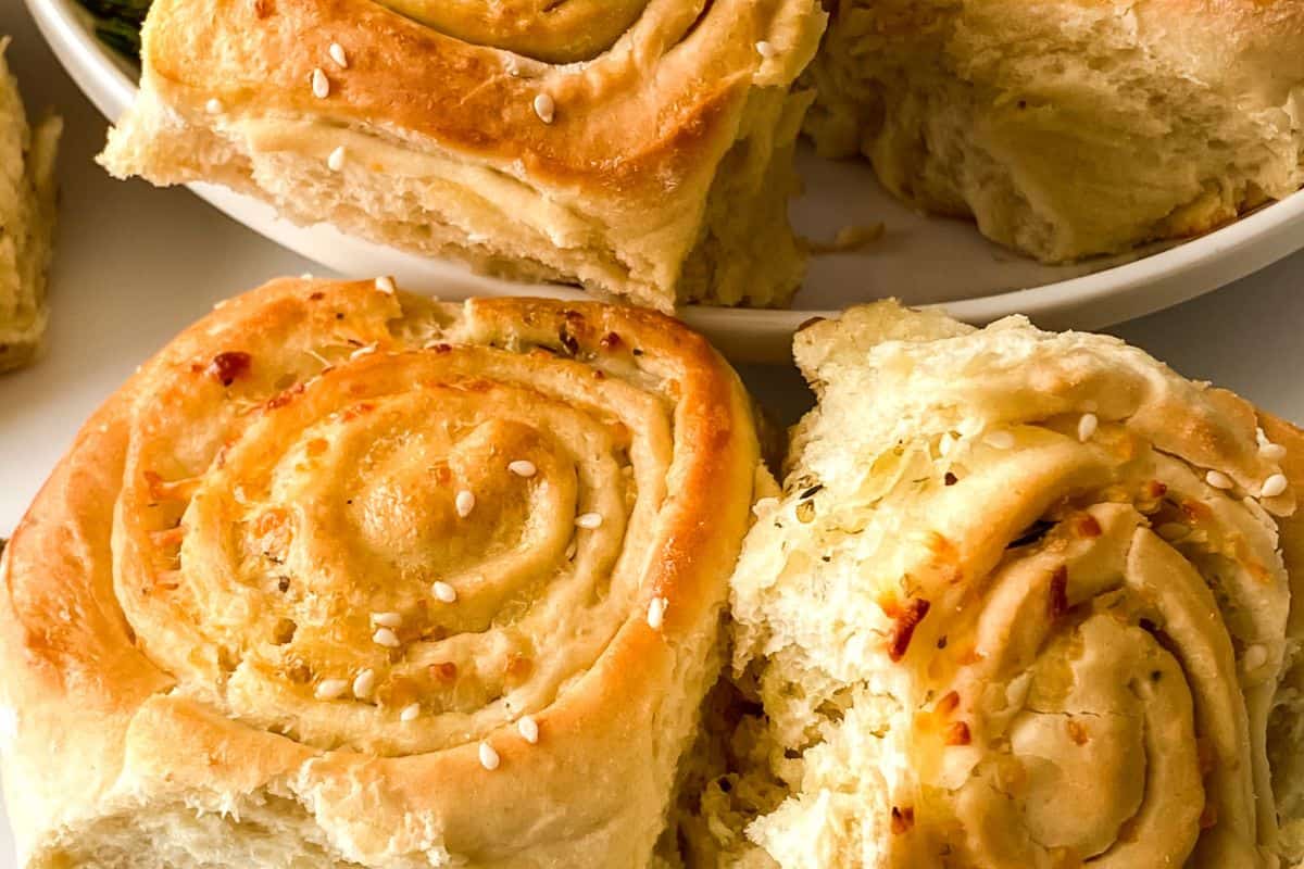 Close-up of freshly baked bread rolls with a spiral pattern, topped with sesame seeds, on a white plate—a must try for fans of quick breads you can bake anytime.