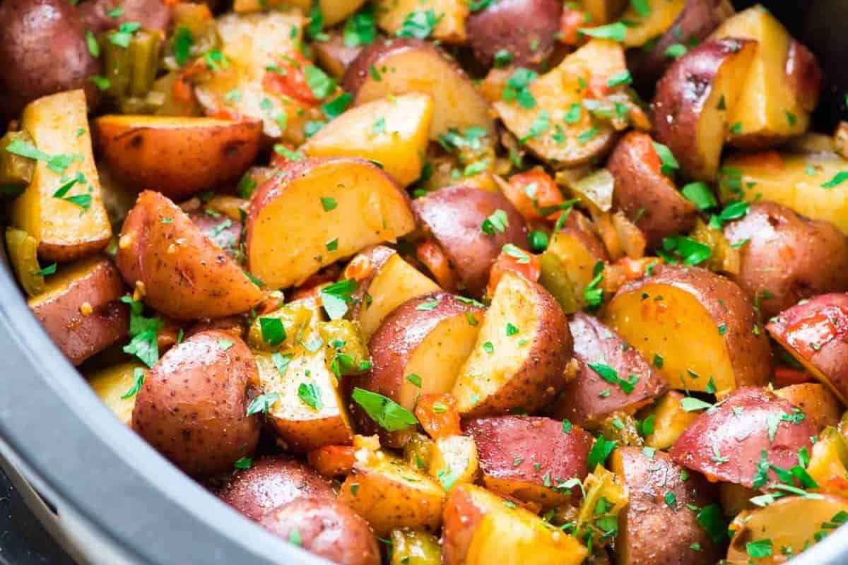 A close-up of cooked red potatoes mixed with chopped green herbs and vegetables in a slow cooker—perfect for easy slow cooker breakfasts on busy mornings.