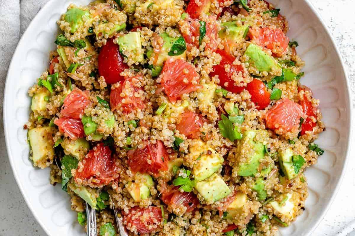 A bowl of quinoa salad with diced avocado, grapefruit segments, cherry tomatoes, chopped herbs, and a light dressing—perfect for those seeking fresh and vibrant grapefruit recipes.