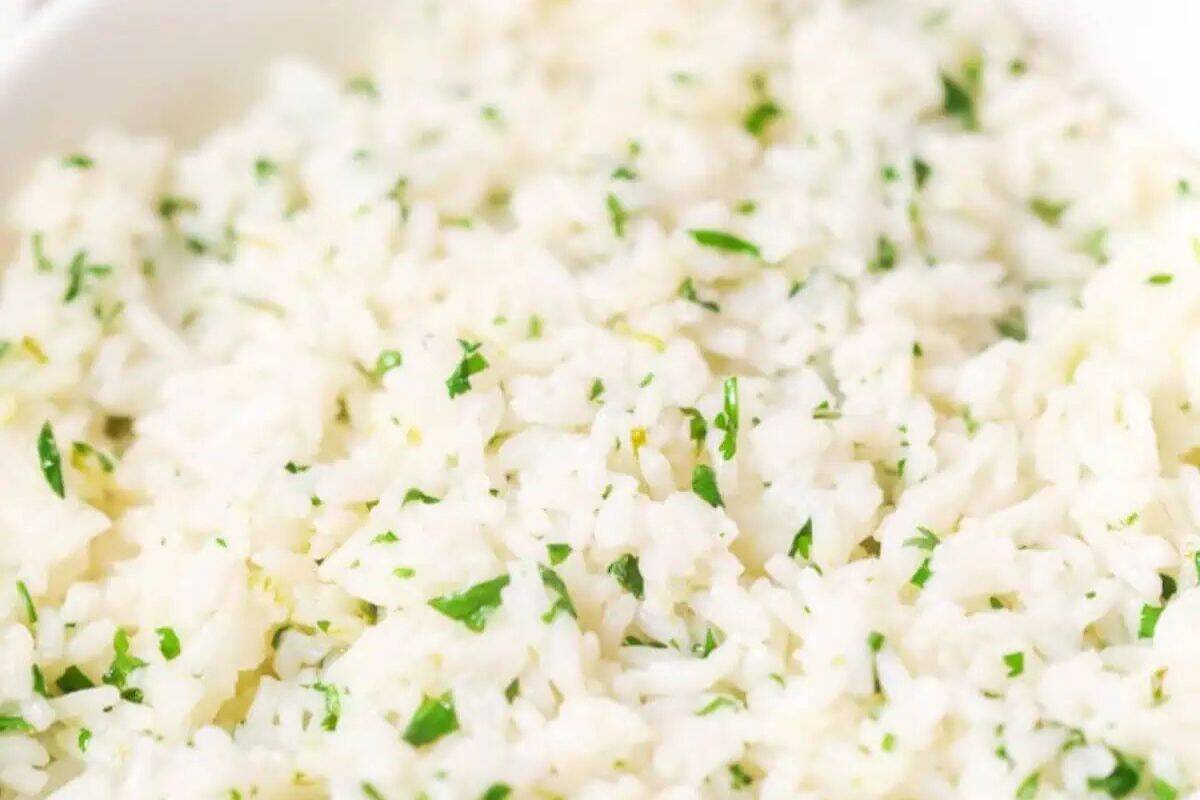 Close-up of cooked white rice mixed with finely chopped green herbs on a white plate, perfect for delicious recipes or enhanced with a squeeze of fresh lime.
