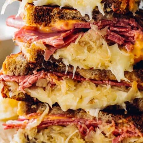 A stack of gourmet Reuben sandwiches filled with corned beef, sauerkraut, melted Swiss cheese, and dressing between slices of toasted rye bread creates a visually appealing and tasty treat.