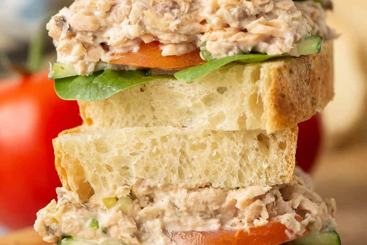 A stacked salmon salad sandwich with two slices of bread, a layer of salmon salad, lettuce, and tomato visible.