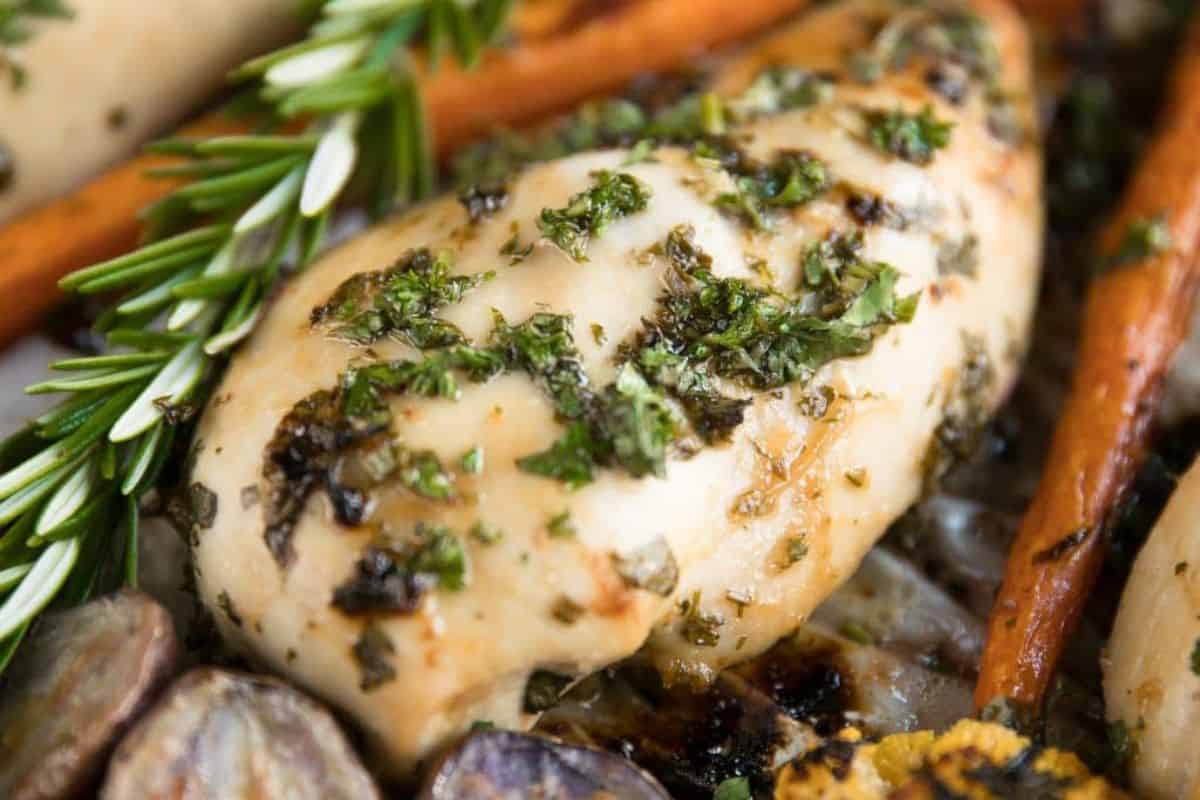 Close-up of a cooked chicken breast seasoned with herbs, surrounded by roasted carrots, potatoes, and a sprig of rosemary—an inviting dish that pairs perfectly with refreshing grapefruit recipes.