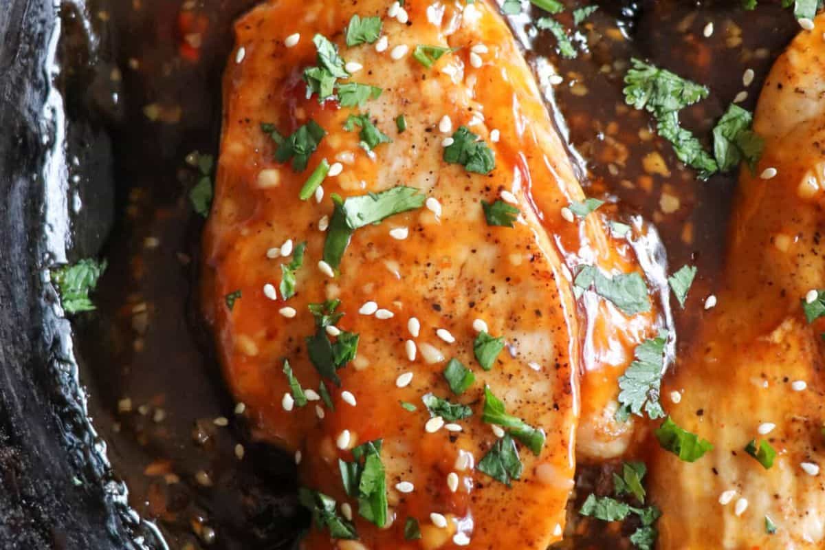 Close-up of cooked chicken breast topped with sauce, chopped cilantro, fresh lime, and sesame seeds in a skillet—a vibrant scene for anyone who loves delicious recipes and creative cooking.