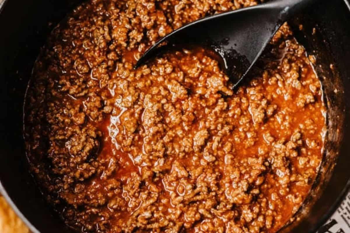 Cooked ground beef simmering in a tomato-based sauce in a Dutch oven, with a black serving spoon resting on the side—a classic for hearty recipes.