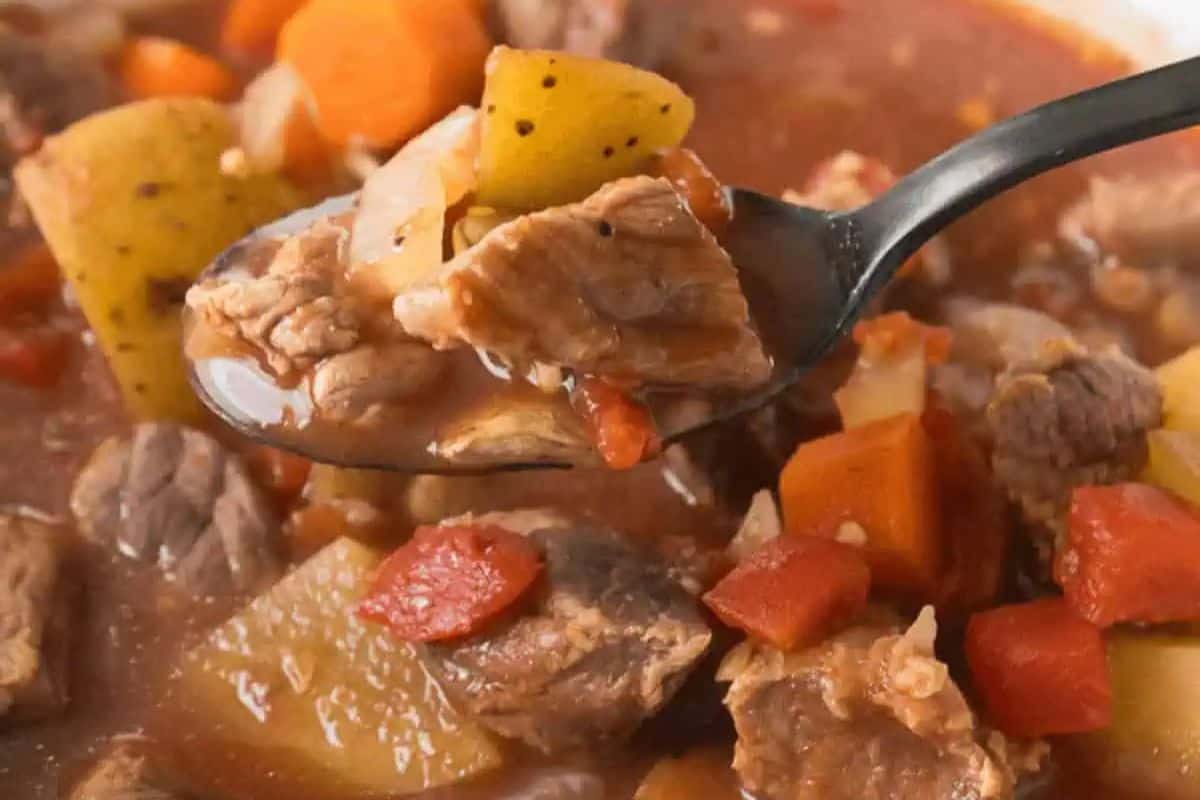 A close-up of a comforting spoonful of beef stew with chunks of beef, potatoes, carrots, and tomatoes in a broth—perfect for your dinner rotation or to inspire new beef soup recipes.