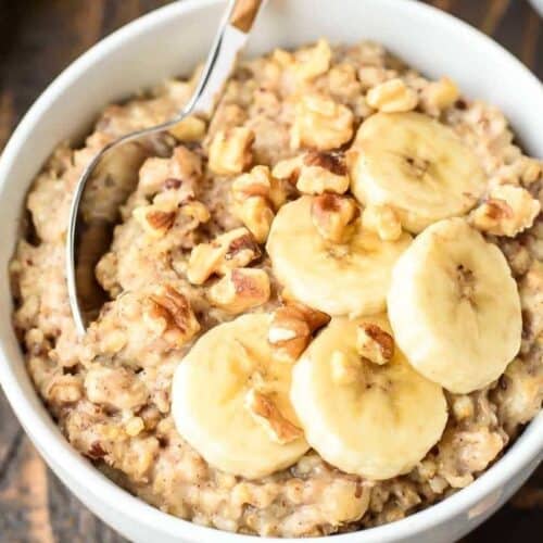 A bowl of oatmeal topped with banana slices and chopped walnuts, perfect for busy mornings. This wholesome dish is a great addition to your breakfast recipes, with a spoon resting inside the bowl.