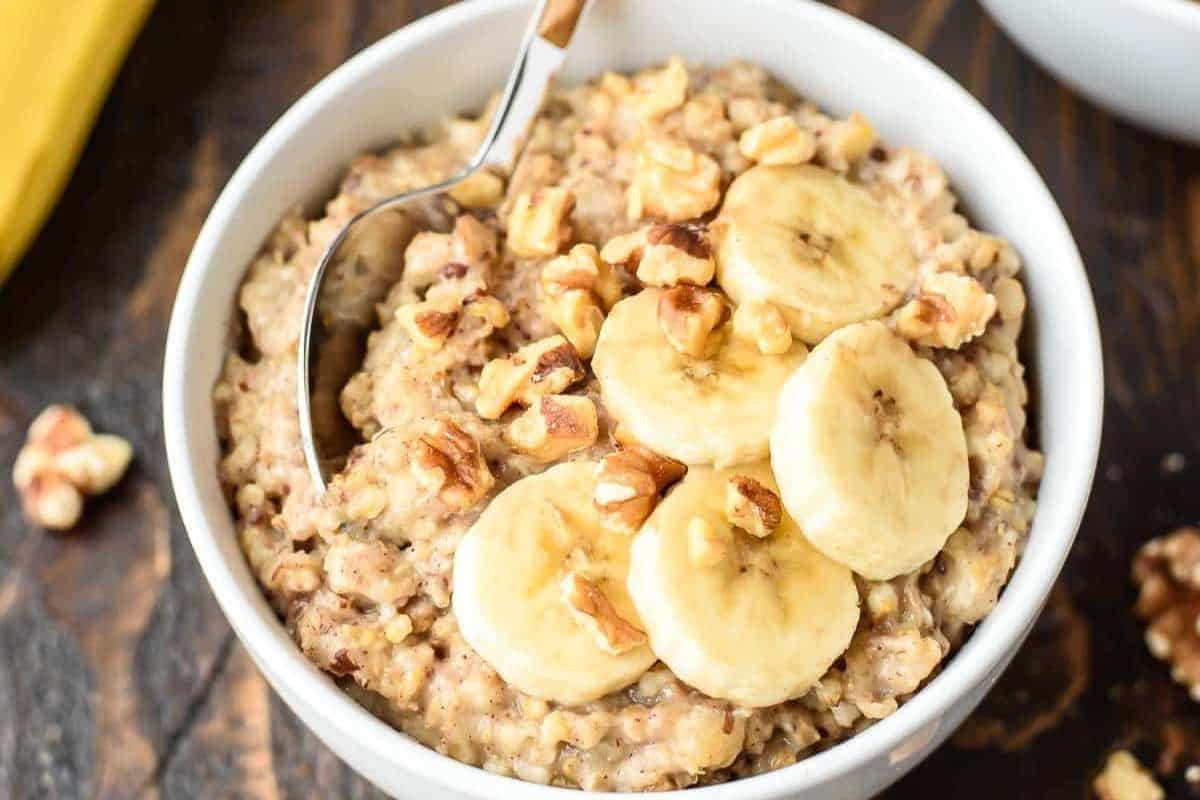 A bowl of oatmeal topped with banana slices and chopped walnuts, perfect for busy mornings. This wholesome dish is a great addition to your breakfast recipes, with a spoon resting inside the bowl.