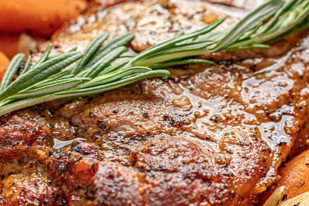 Close-up of a cooked, seasoned Delicious Pork Roast topped with a sprig of fresh rosemary.