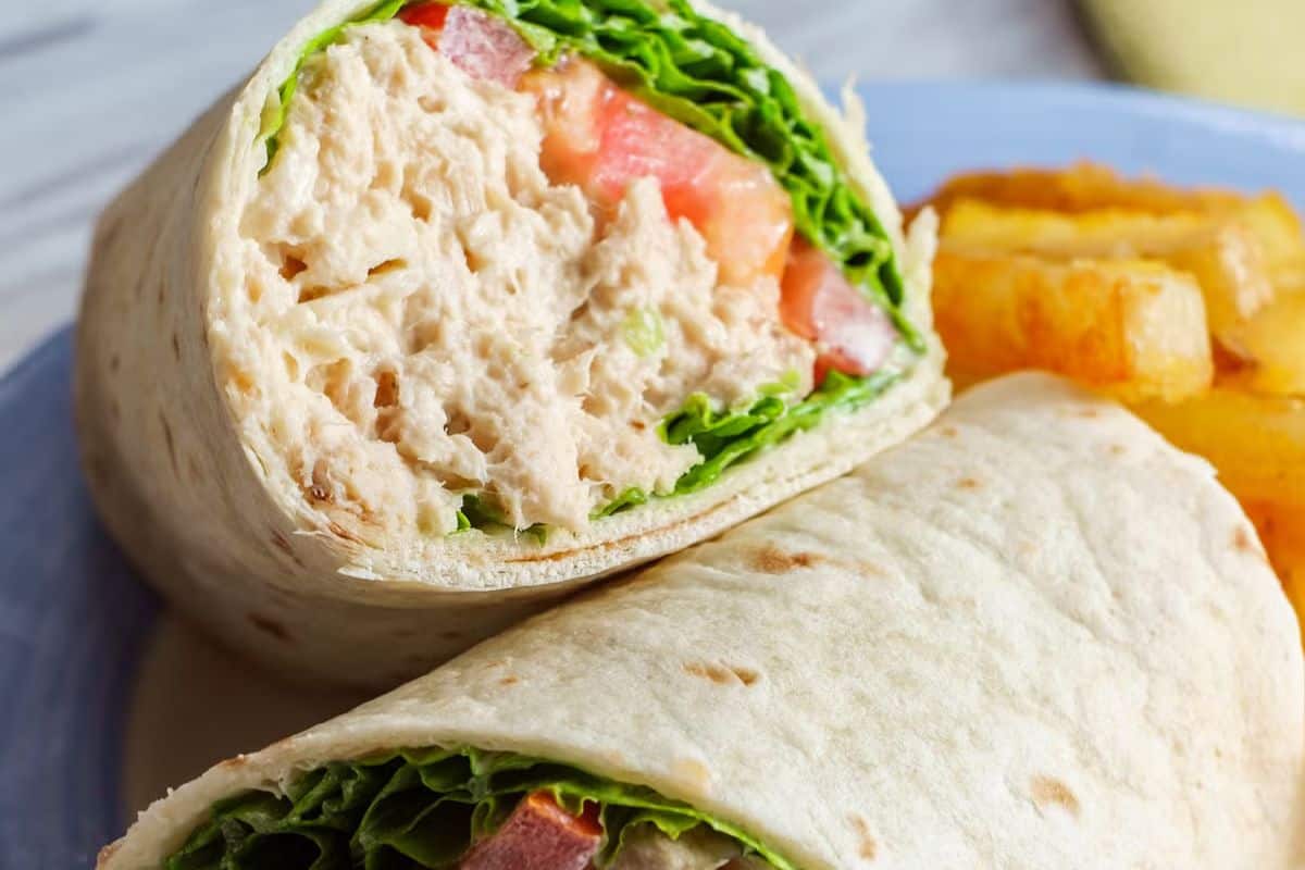 A close-up of a tuna salad wrap with lettuce and tomato, cut in half, served with a side of potato wedges—a perfect example of easy tuna meals for a simple yet satisfying dinner.