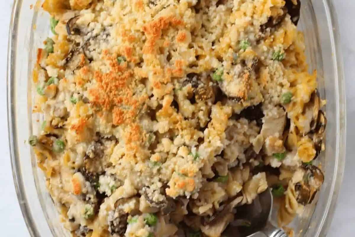 A baked casserole in a clear glass dish topped with a golden breadcrumb and cheese crust, this classic tuna dinner combines mixed vegetables, noodles, and canned tuna for a comforting meal.