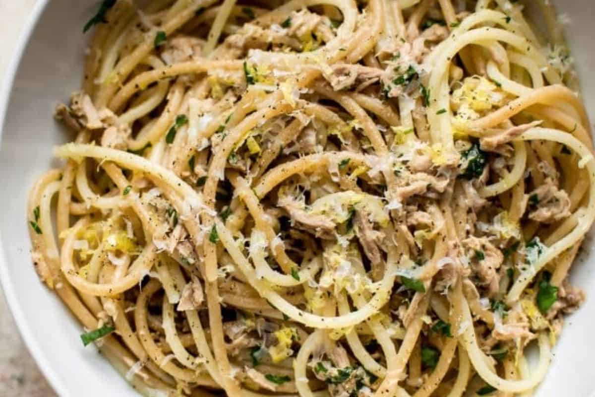 A bowl of spaghetti mixed with tuna, grated cheese, chopped herbs, and black pepper—perfect for easy tuna meals or a quick canned tuna dinner.