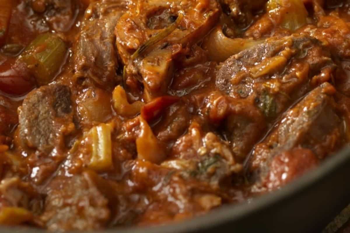 Close-up of a beef stew with chunks of meat, tomatoes, celery, and onions in a thick, reddish-brown sauce—one of the ultimate Dutch oven recipes for hearty meals.