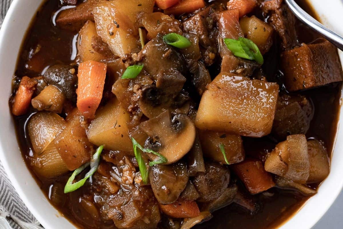 A comforting bowl of beef stew with chunks of potatoes, carrots, mushrooms, and green onion slices in a rich brown broth—perfect for dinner or when you’re searching for hearty beef soup recipes.