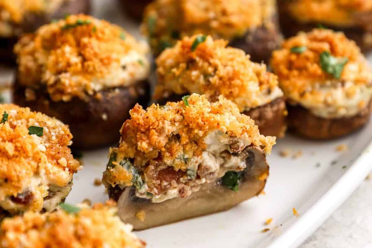 Stuffed mushrooms topped with golden breadcrumbs and herbs are arranged on a white plate—an irresistible addition to your favorite stuffed mushroom recipes.