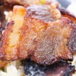 Close-up of crispy, browned slices of baked pork belly served on a bed of white rice.