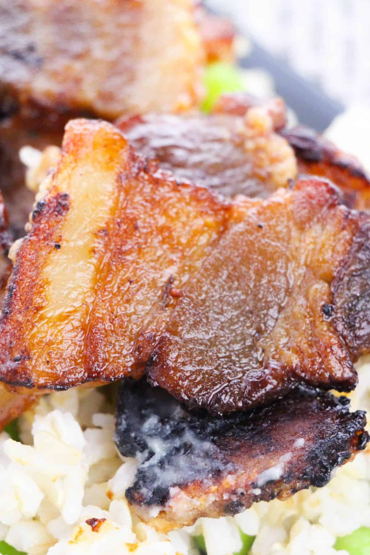 Close-up of crispy, browned slices of baked pork belly served on a bed of white rice.
