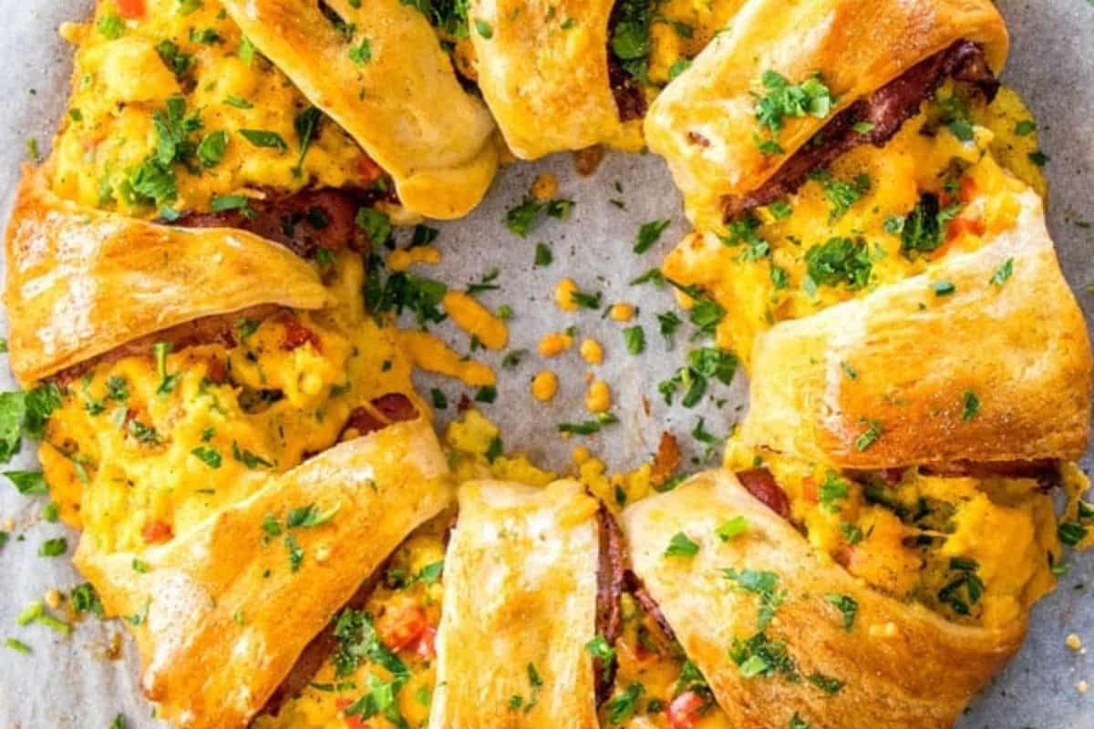 A baked crescent ring filled with scrambled eggs, bacon, and cheese, garnished with chopped parsley—perfect for cozy Christmas breakfast gatherings and festive Christmas morning recipes. Displayed on a parchment-lined surface.