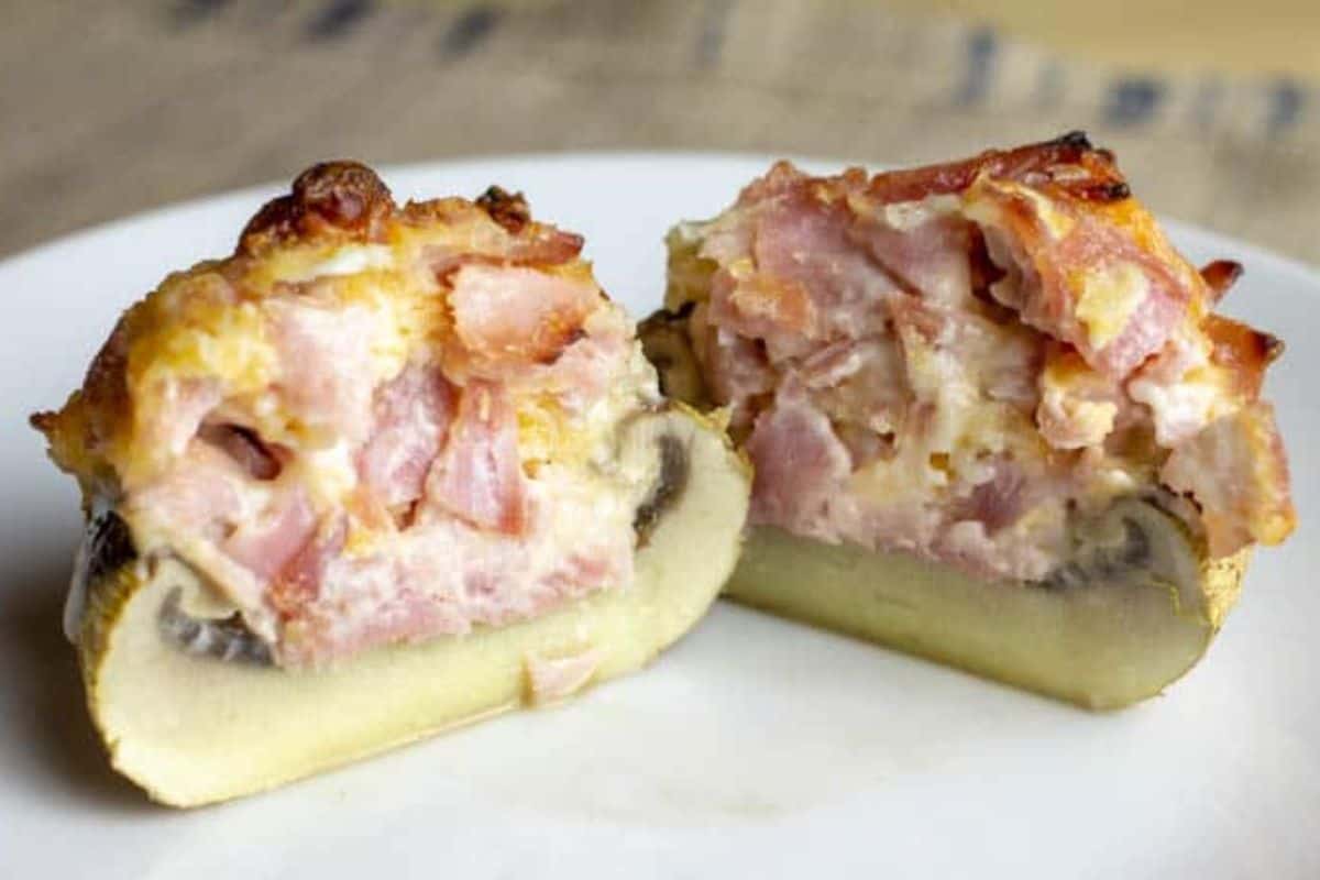 A large stuffed mushroom cap filled with diced ham and melted cheese, cut in half to reveal the savory stuffing, served on a white plate—perfect for fans of delicious stuffed mushroom recipes.