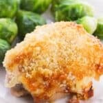 A Hellman's Crusted Parmesan Chicken thigh, breaded and baked to perfection, is served on a white plate alongside several steamed Brussels sprouts.