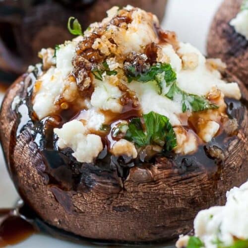 Close-up of a stuffed mushroom cap topped with crumbled cheese, chopped herbs, and a drizzle of dark balsamic glaze—perfect for fans of delicious stuffed mushroom recipes.