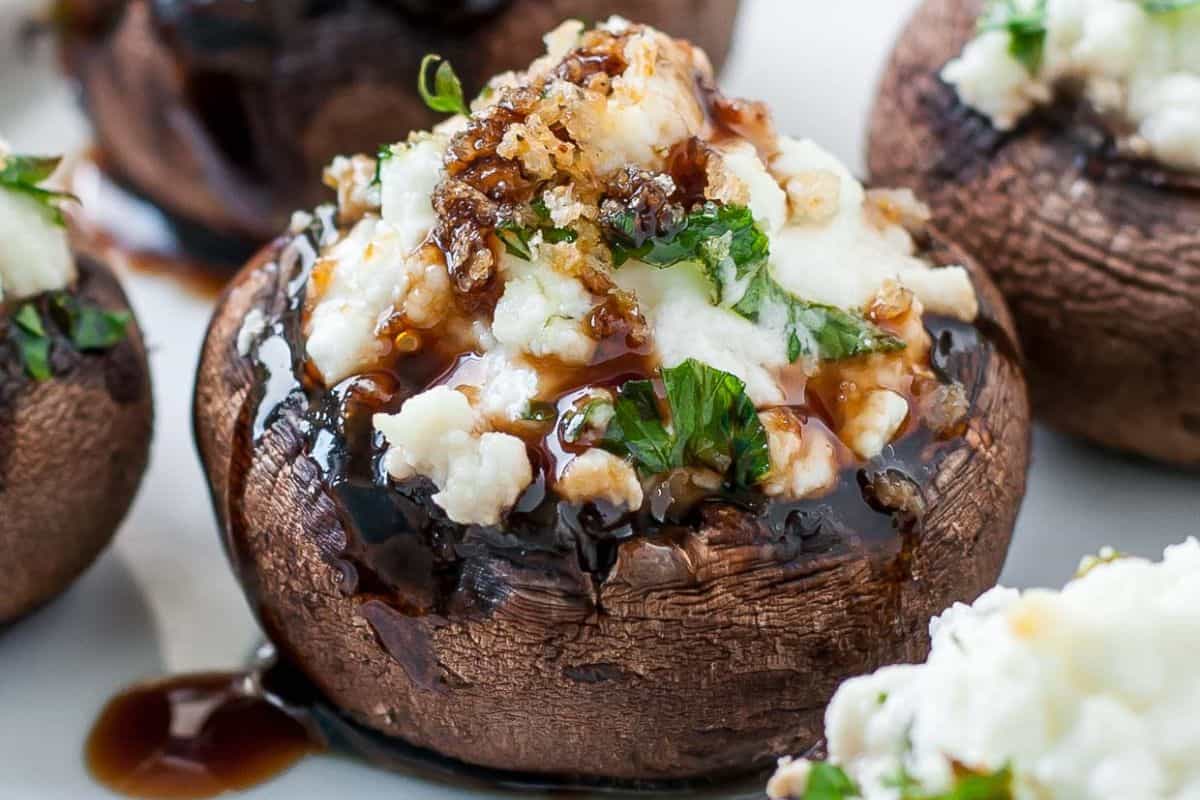 Close-up of a stuffed mushroom cap topped with crumbled cheese, chopped herbs, and a drizzle of dark balsamic glaze—perfect for fans of delicious stuffed mushroom recipes.