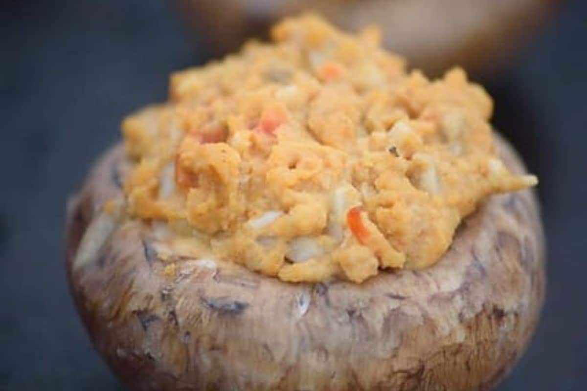 A close-up of a mushroom cap filled with an orange, crumbly stuffing containing small pieces of vegetables—perfect inspiration for your next stuffed mushroom recipes.